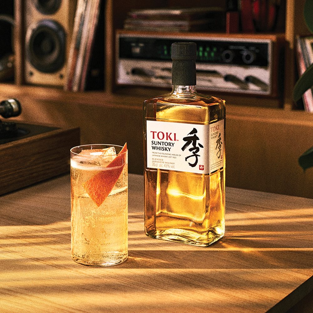 A Toki highball beside a bottle of Suntory Toki whisky in a warmly lit home bar.