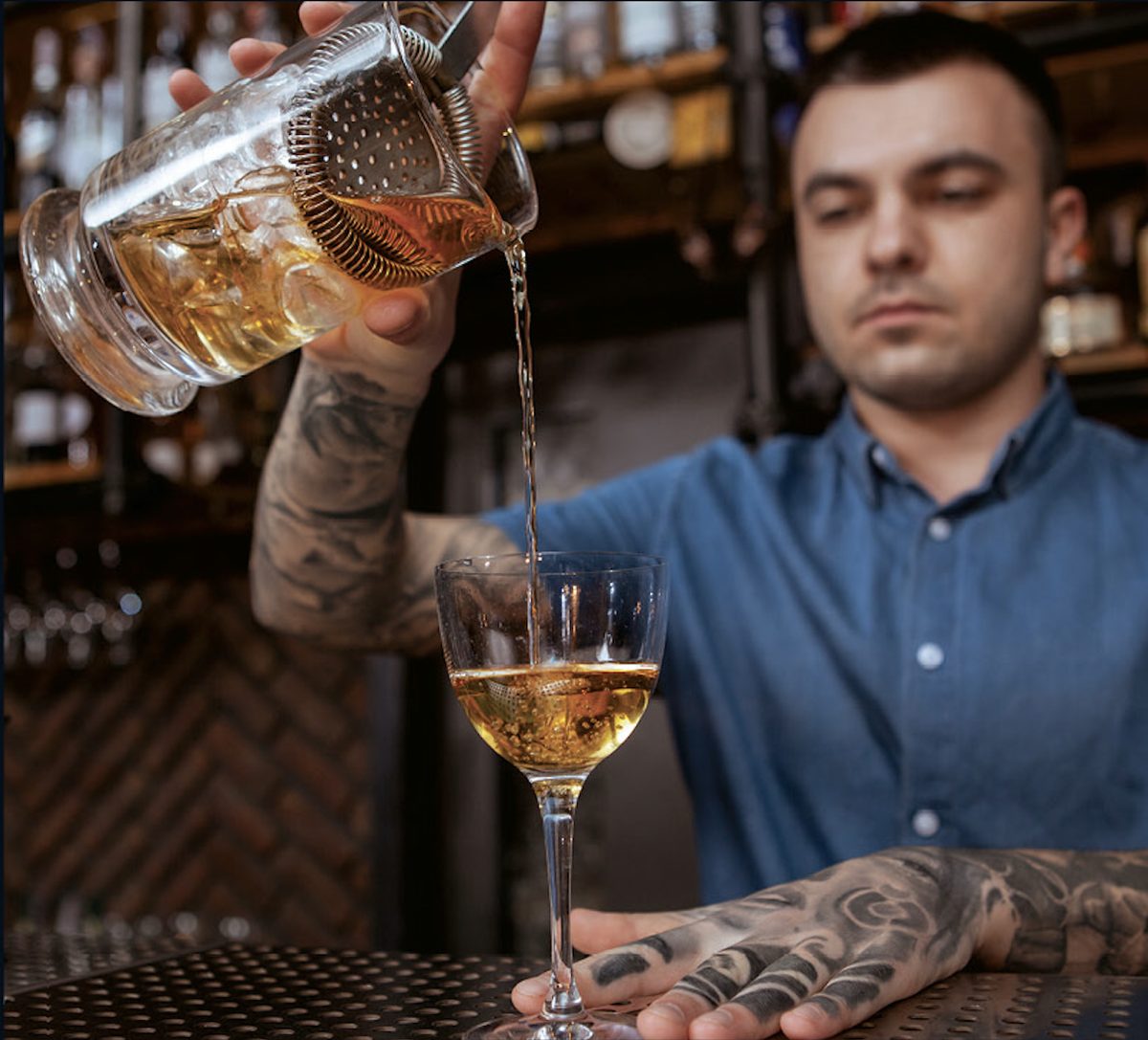 A bartender straining a cocktail from a mixing glass into a chilled coupe.