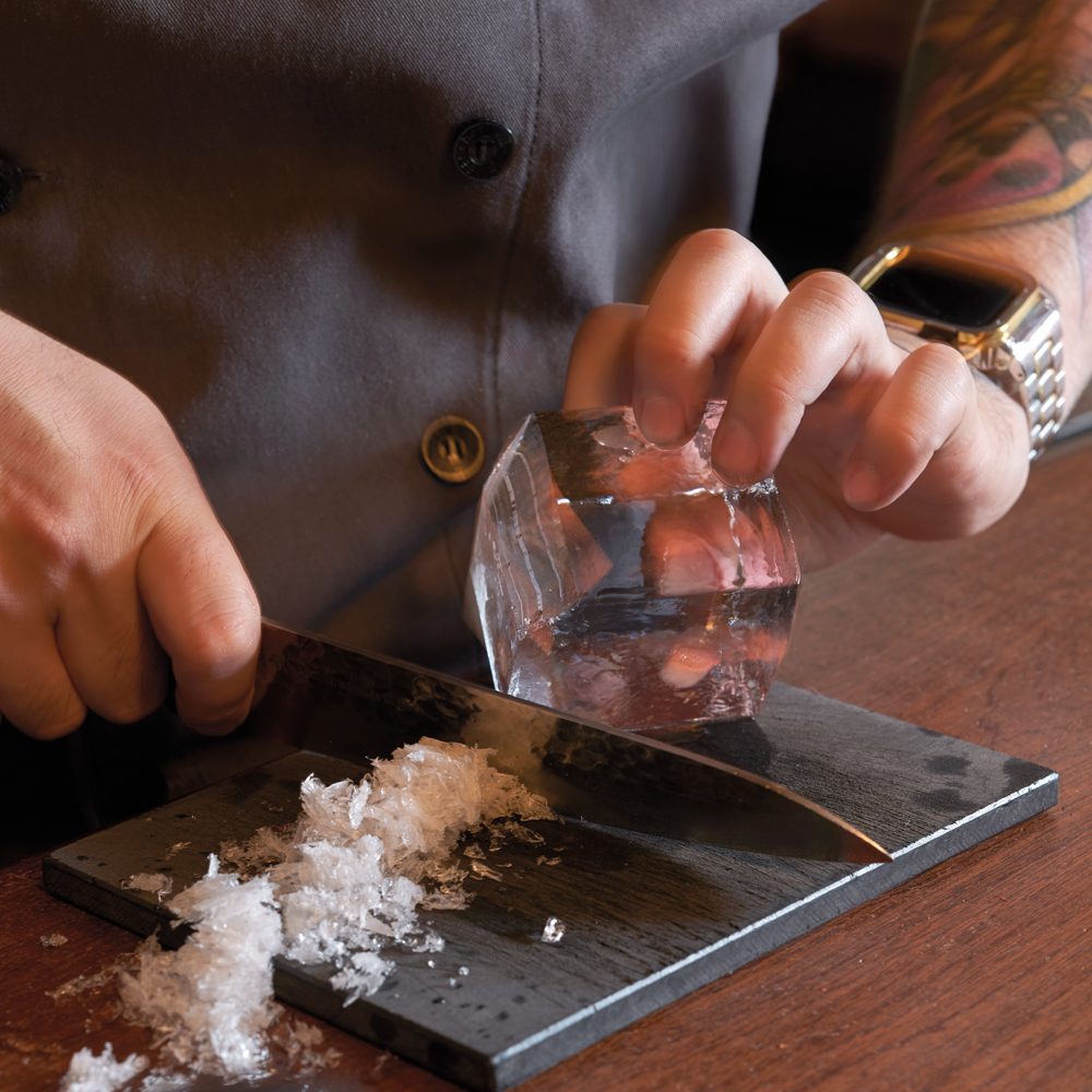 A bartender hand-carving a block of clear ice.