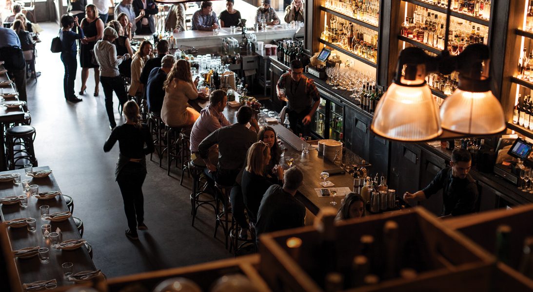 A busy, warmly lit bar full of people talking over drinks.